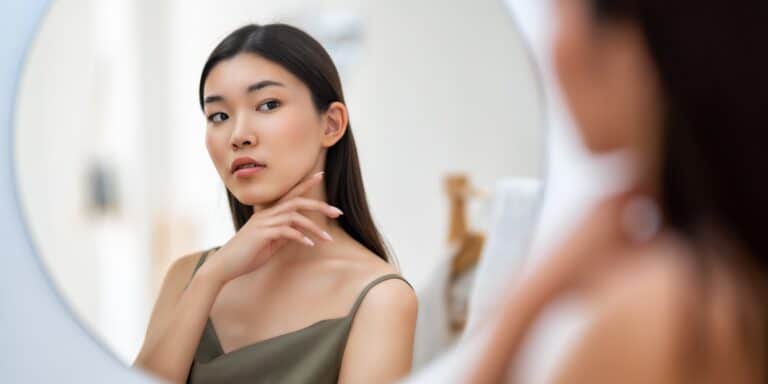 Woman examining her face in a mirror, related to laser facial vein removal.
