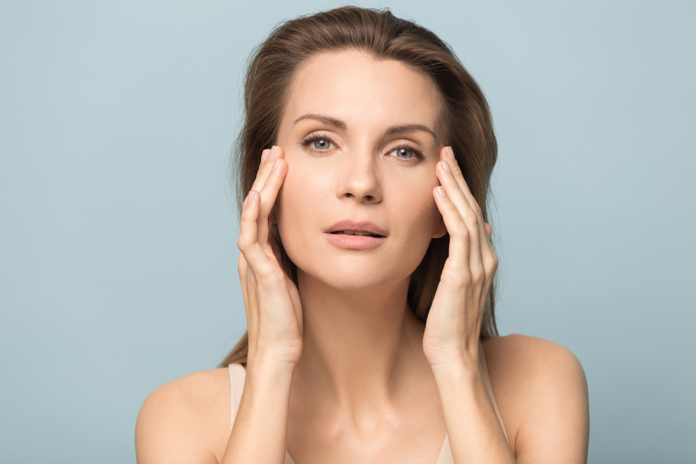 Woman touching her face, illustrating skin care benefits.