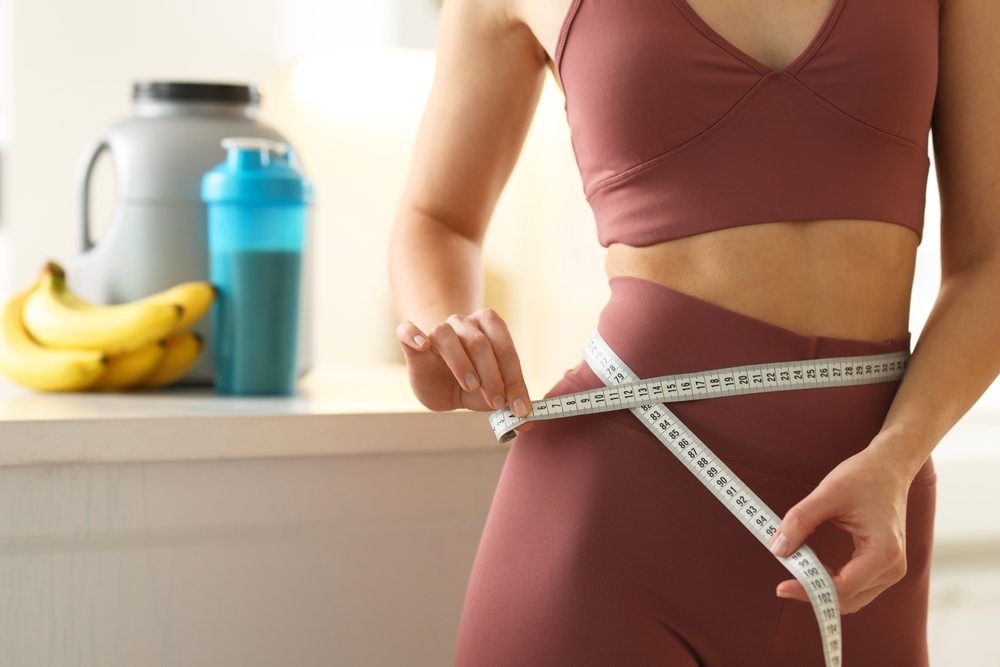 Person measuring waist with tape, related to Vanquish ME treatment.
